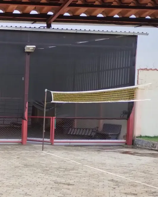 Quadra de piso calçado com rede de vôlei armada diante de um galpão coberto